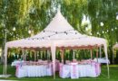Festlich dekorierter rosa Pavillon mit runden Tischen und Stuehlen, umgeben von Lichterketten im gruenen Garten