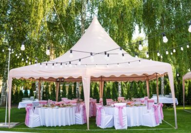 Festlich dekorierter rosa Pavillon mit runden Tischen und Stuehlen, umgeben von Lichterketten im gruenen Garten