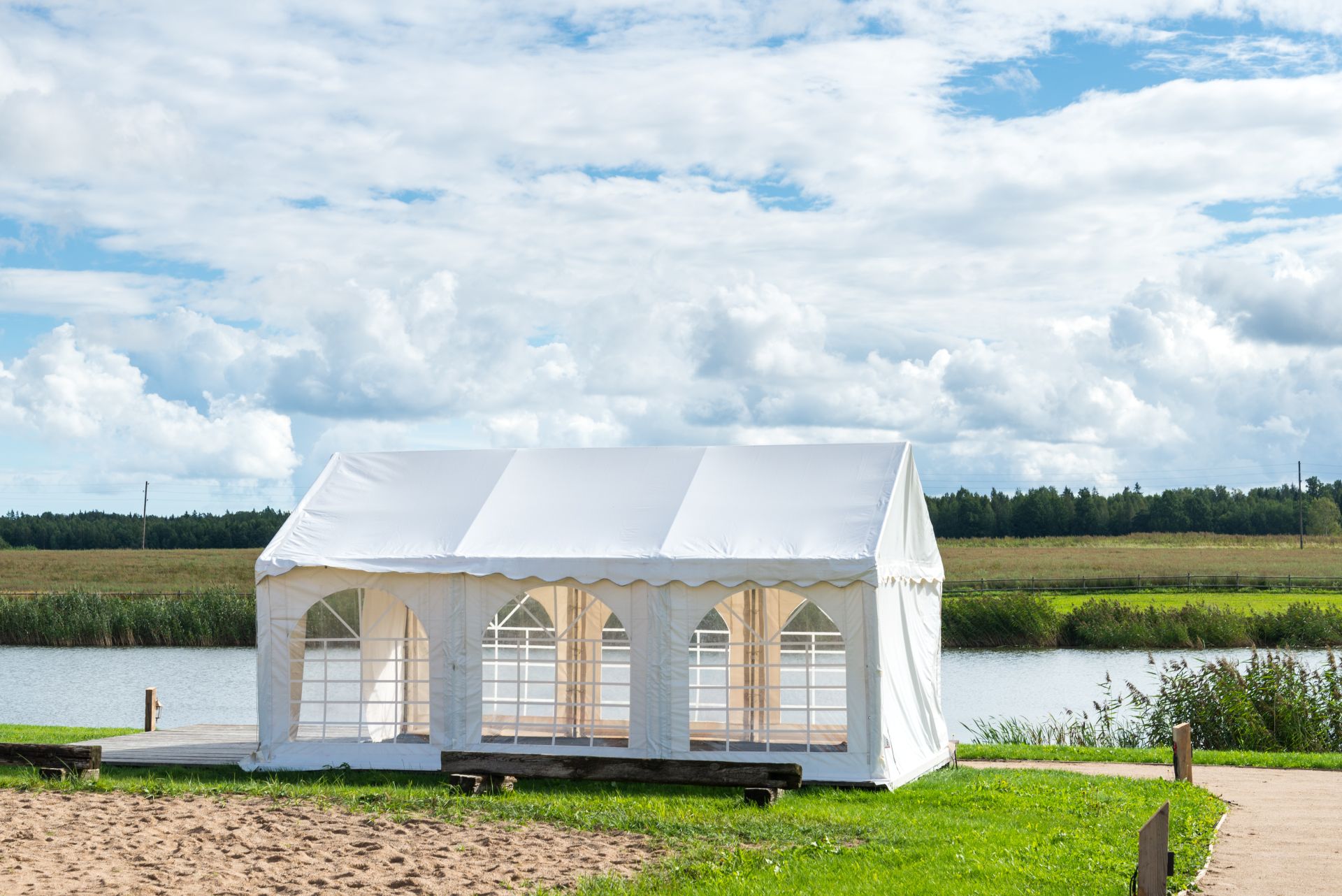 Weißer Pavillon mit Fenstern an einem Seeufer unter blauem Himmel