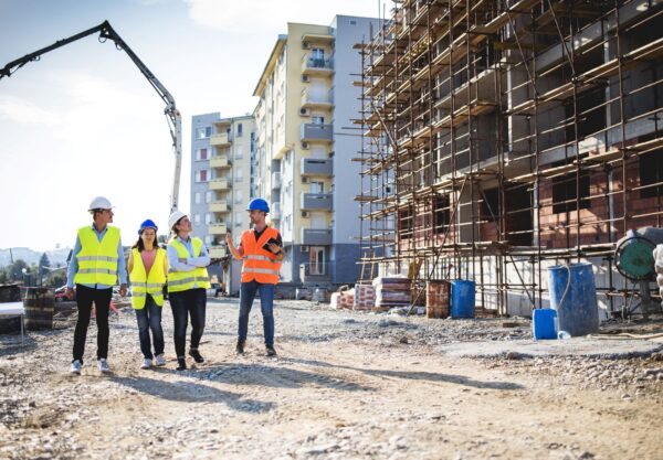 Gruppe von Bauleitern und Ingenieurinnen im Gespraech auf einer stadtnahen Baustelle – Einsatzort fuer mobile Schallschutzsysteme im Wohngebiet