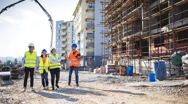 Gruppe von Bauleitern und Ingenieurinnen im Gespraech auf einer stadtnahen Baustelle – Einsatzort fuer mobile Schallschutzsysteme im Wohngebiet